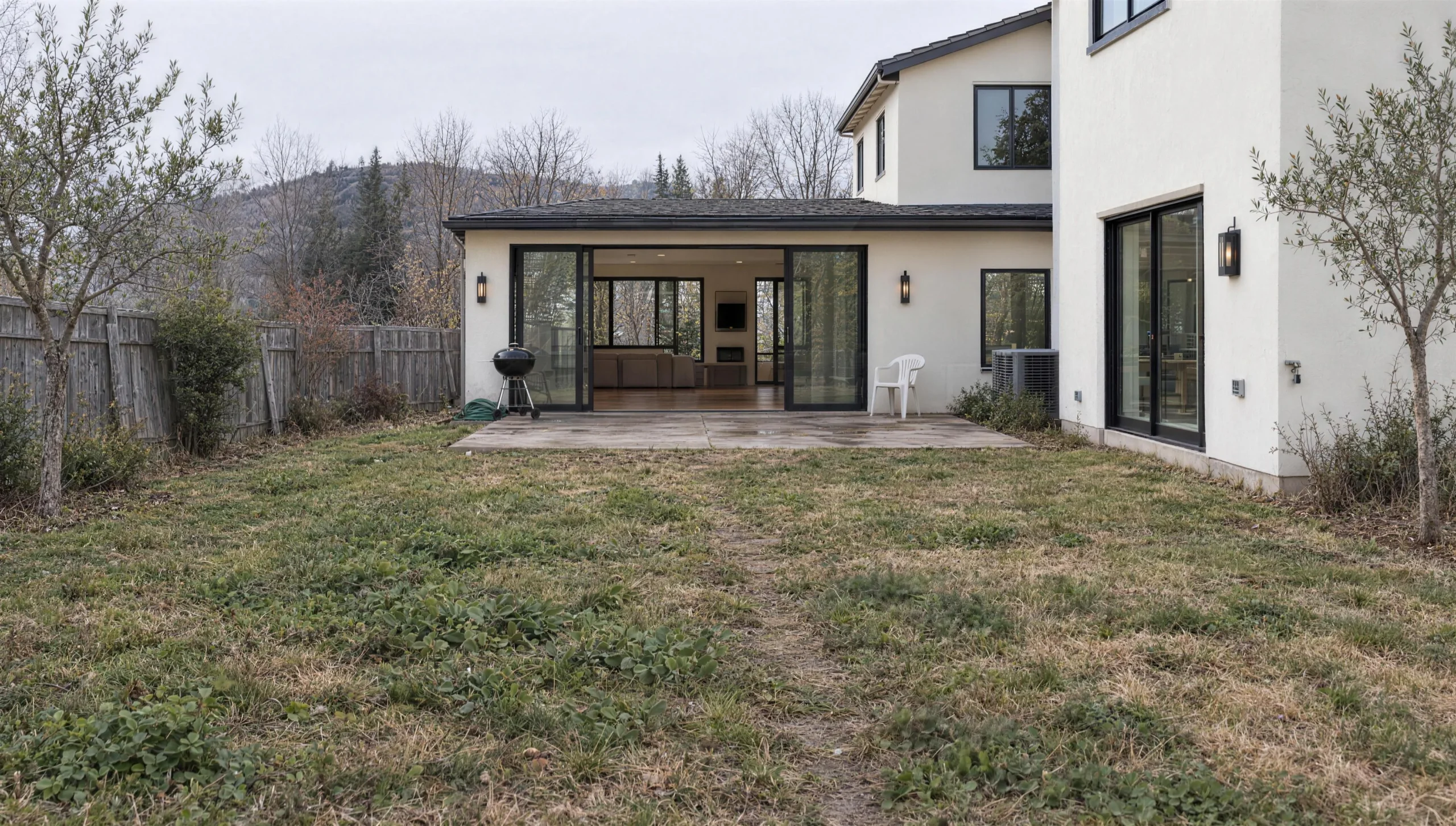 The same backyard a year before the remodel on a grey winter day: a tired lawn, young olive trees and a small concrete patio